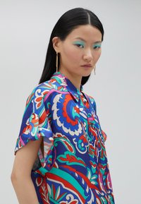 Camisa de botones de manga corta colorida con un patrón floral y de paisley en azul, rojo y verde. Tejido suave con un corte relajado.