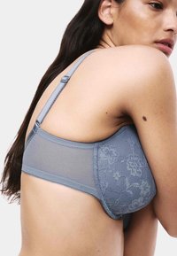 Šedé krajkové spodní prádlo s pletivovým zadním dílem, vybavené nastavitelnými ramínky a květinovými motivy, zdůrazňující hladkou texturu a přiléhavý střih.