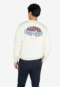 Kremowa bluza z dużą, wielokolorową grafiką na plecach z napisem "HARPER i NEYER". Ribnowe mankiety i dół.