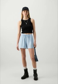 Black sleeveless top, light blue striped shorts with drawstring, black cap, black ankle boots, white socks, small blue bag.