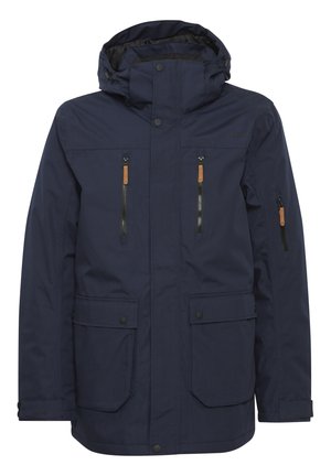 Giacca impermeabile blu navy con cappuccio, dotata di due tasche superiori con zip, due tasche inferiori con patta e dettagli in pelle marrone chiaro sulle cerniere.