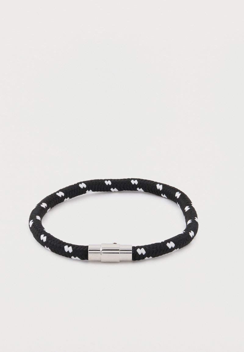 Μαύρο και άσπρο πλεκτό βραχιόλι με μοτίβο και λαμπερό ασημένιο μαγνητικό κούμπωμα, τοποθετημένο σε απλό λευκό φόντο.