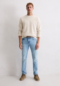 Jasnobeżowy sweter o fakturze, jasnoniebieskie dżinsy i brązowe buty zamszowe. Krój o prostych nogawkach, dekolt w łódkę, proste zdobienia na swetrze.