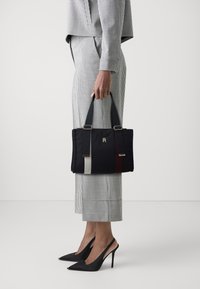 Granatowa torba na ramię wykonana z pikowanej tkaniny, z pionowymi paskami w kolorze szarym i bordowym, wyposażona w dwa solidne uchwyty do noszenia oraz złote elementy dekoracyjne.