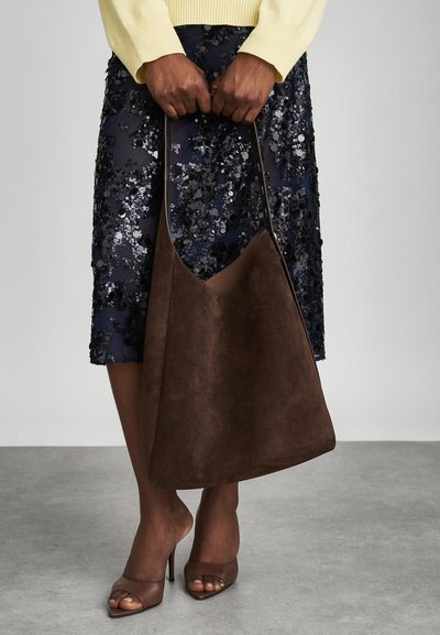 Sac en daim marron au toucher doux et à large ouverture, associé à une jupe en sequins bleu marine et des talons ouverts marron.