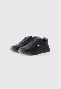 Black leather sneakers with a textured surface, round toe, flat rubber sole, and logo patch featuring red, white, and blue colors on the side.
