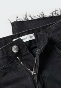 Jean en denim noir avec un ourlet effiloché, équipé d'un bouton métallique et d'une fermeture éclair. Étiquette visible avec les informations sur la taille et la marque.