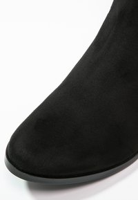 Černé semišové kotníkové boty s špičatou špičkou a hladkou strukturou, s úzkou gumovou podrážkou a žádnými viditelnými kovovými prvky nebo dekoracemi.