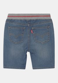 Farkkuhousut, joissa on harmaa joustava vyötärö, jossa on punainen raita. Takataskuissa on koristeelliset ompeleet; Levi's-logo-tunnus on läsnä.