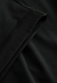 Close-up of black fabric with detailed stitching and smooth texture, highlighting a folded seam on a garment.