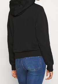 Sudadera negra con capucha ajustable, puños y dobladillo acanalados. Combinada con jeans de mezclilla azul con un diseño clásico de cinco bolsillos.