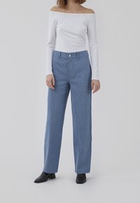 Modré vzorované kalhoty s širokými nohavicemi z texturované látky, s knoflíkovým zapínáním a dvěma předními kapsami, doplněné bílou košilí bez ramene.