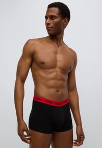 Μαύρο εσώρουχο τύπου μποξέρ με κόκκινη λάστιχη μέση με λογότυπο. Διαθέτει στενή εφαρμογή και απαλή υφή, τονίζοντας την άνετη εφαρμογή.