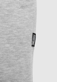 Pantalones de chándal grises hechos de una tela suave, con un bolsillo lateral y una etiqueta negra con texto blanco. Diseño simple con un ajuste cómodo.