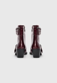 Burgunderfarbene Leder Stiefeletten mit einem stabilen Absatz, einem Schnallenakzent und Reißverschluss; glatte Oberfläche mit subtilen Nähdetails.
