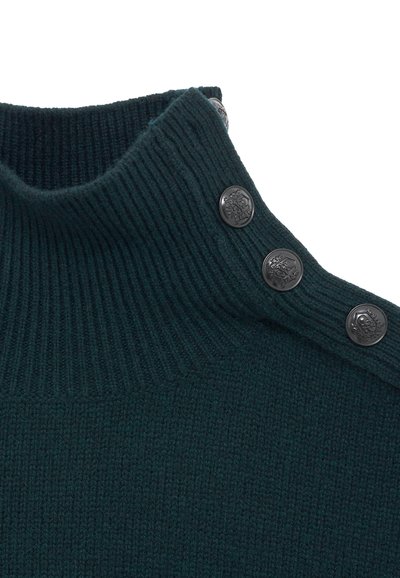 Mørkegrøn strikket sweater med en høj ribbet krave, der har fire skinnende sorte knapper langs skulderen som detalje.