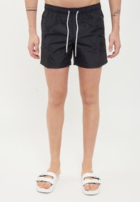 Costumi da bagno neri realizzati in materiale leggero, con vita elastica e cordoncino bianco. Indossati con sandali bianchi caratterizzati da due cinghie.
