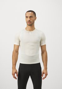Haut ajusté beige clair à manches courtes avec col rond, texture lisse et design minimaliste, associé à un pantalon noir ajusté.