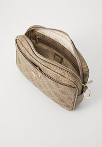 Gold-textured cosmetic bag with a zippered closure, patterned exterior, and logo detail. Interior lined with beige fabric featuring a repeated logo design.