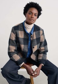 Tumesinises ja beežis ruuduline villane jope, ümmarguse kaelusega, nööpidega kinnitatav ja kontrastse musta äärisega. Sobitatud sinise sametise särgiga.