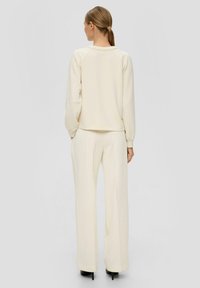 Crème-kleurige sweatshirt met een ronde halslijn en raglanmouwen, gecombineerd met bijpassende geribbelde wijde broekspijpen. Gladde textuur, minimaal ontwerp.