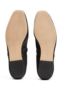 Zapatos de cuero negro con una textura suave, con una suela de goma beige y un sutil detalle de costura. Marca del fabricante visible en la suela.