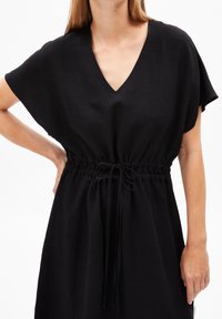 Czarna sukienka z dekoltem w serek, krótkimi rękawami i elastycznym pasem ze sznurkiem. Wykonana z lekkiego materiału o gładkiej fakturze.