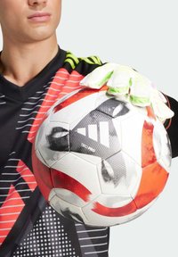 Pallone da calcio con design rosso, bianco e nero, caratterizzato da pannelli testurizzati. Mano guantata che tiene il pallone, indossando una maglietta nera con accenti rossi.