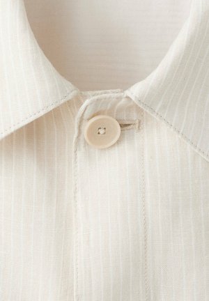 Primer plano de un cuello de camisa beige con textura y un solo botón beige abrochado a través de un ojal.