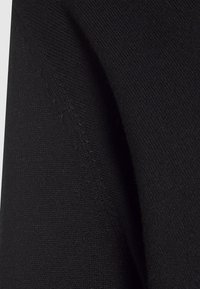 Close-up of black knitted fabric with visible seam stitching and textured weave pattern.