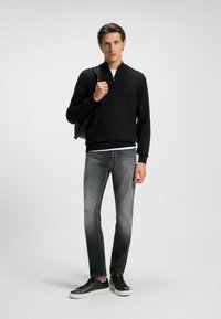 Maglione nero con zip sopra una camicia bianca, abbinato a jeans grigi e sneakers nere con suola bianca, caratterizzato da una trama di tessuto liscia.