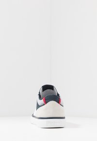Námořnické, šedé a bílé tenisky se semišovou patou. Obsahují červené akcenty na límci a texturovanou gumovou podrážku. Přítomné prošívané detaily.