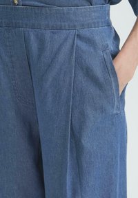 Jeansbroek met een geplooid ontwerp, voorzien van een brede tailleband, zijzakken en een zachte, gestructureerde stof in een middelblauwe kleur.