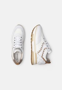 Weiße Sneaker mit strukturierten Paneelen, runden Schnürsenkeln und dekorativen Perforationen. Kontrastierende beige Akzente und eine klobige weiße Sohle.