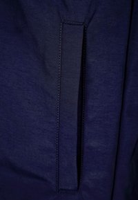 Tmavě modrá látka s hladkou texturou má vertikální rozparek. Okolo okrajů rozparku jsou viditelné detaily šití.