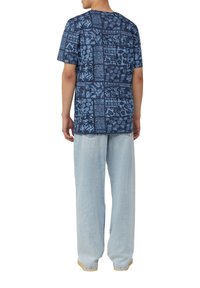 Blauw gemusterde korte mouwen overhemd met bloemen- en geometrische ontwerpen, gecombineerd met lichtblauwe wijdvallende jeans; eenvoudige ronde halslijn.