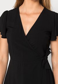Robe noire portefeuille avec des manches courtes à volants, décolleté en V et accent de lien à la taille. Tissu lisse avec un corsage ajusté et une jupe fluide.