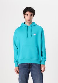 Felpa turchese in cotone misto, presenta una tasca frontale, cordini e una piccola etichetta con logo sul petto. Vestibilità comoda con polsini a costine.