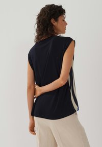 Marinefarbener ärmelloser Oberteil mit rundem Ausschnitt, der an der Seite ein creme- und blaues abstraktes Muster aufweist und eine lockere Passform hat.