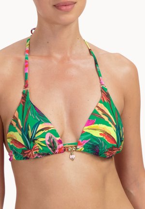 Femme portant un haut de bikini vert à imprimé tropical avec des motifs de feuilles roses, jaunes et orange et un petit pendentif en forme de feuille dorée au centre.