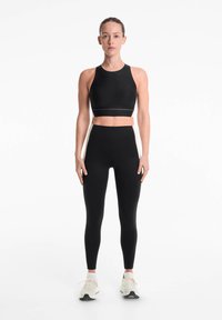 Haut de sport noir à manches courtes et leggings taille haute. Texture lisse, design ajusté et accents blancs sur les côtés des leggings. Chaussures de sport portées.