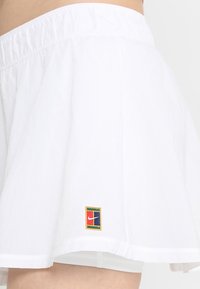 Witte skorts met een gathered elastische tailleband, met een kleine multicolored Nike-logo patch op de onderste zoom. Lichtgewicht stof, uitlopende desig.