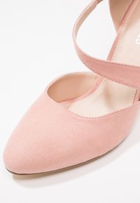 Chaussure en daim rose clair à bout pointu avec une bride unique traversant l'avant et un talon bas, vue de dessus sur fond blanc.