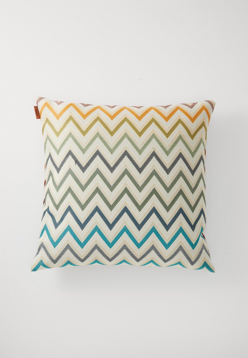 Square cushion featuring a zigzag pattern in orange, green, gray, and blue against a cream background; textured fabric with a side tag.