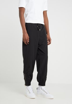 Black lightweight jogger pants with elastic waistband, drawstring, and zippered cuffs. Paired with white sneakers and a white shirt.
