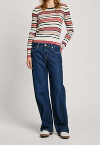 Chemise à manches longues rayée aux nuances de rose, bleu et vert ; associée à un jean large bleu foncé ; baskets blanches décontractées.