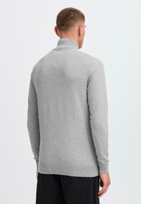 Grå pullov sweater med hög krage, långa ärmar, ribbad nederkant och mudd. Tyget verkar mjukt med en jämn textur.