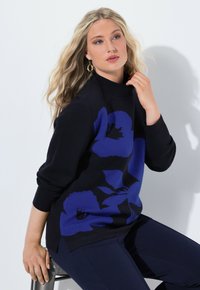 Maglione nero con grandi motivi floreali blu, design semi-attillato, collo alto, polsini a coste, abbinato a pantaloni scuri, texture liscia.