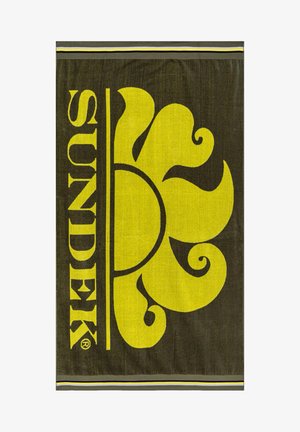La toalla presenta un fondo oscuro con un gran diseño floral amarillo y el texto "SUNDEK". Tejido texturizado con un acento a rayas en la parte inferior.