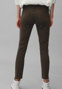 Pantaloni marroni slim-fit con una texture liscia, dotati di due tasche posteriori e vita medio-alta, abbinati a sneakers bianche alte fino alla caviglia.